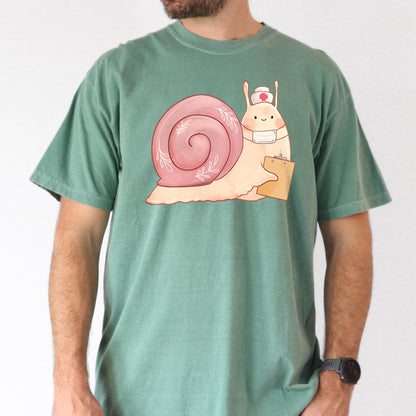 Man wearing light green t-shirt with an illustration of  snail holding a clipboard and wearing a nurse's hat and face mask.
