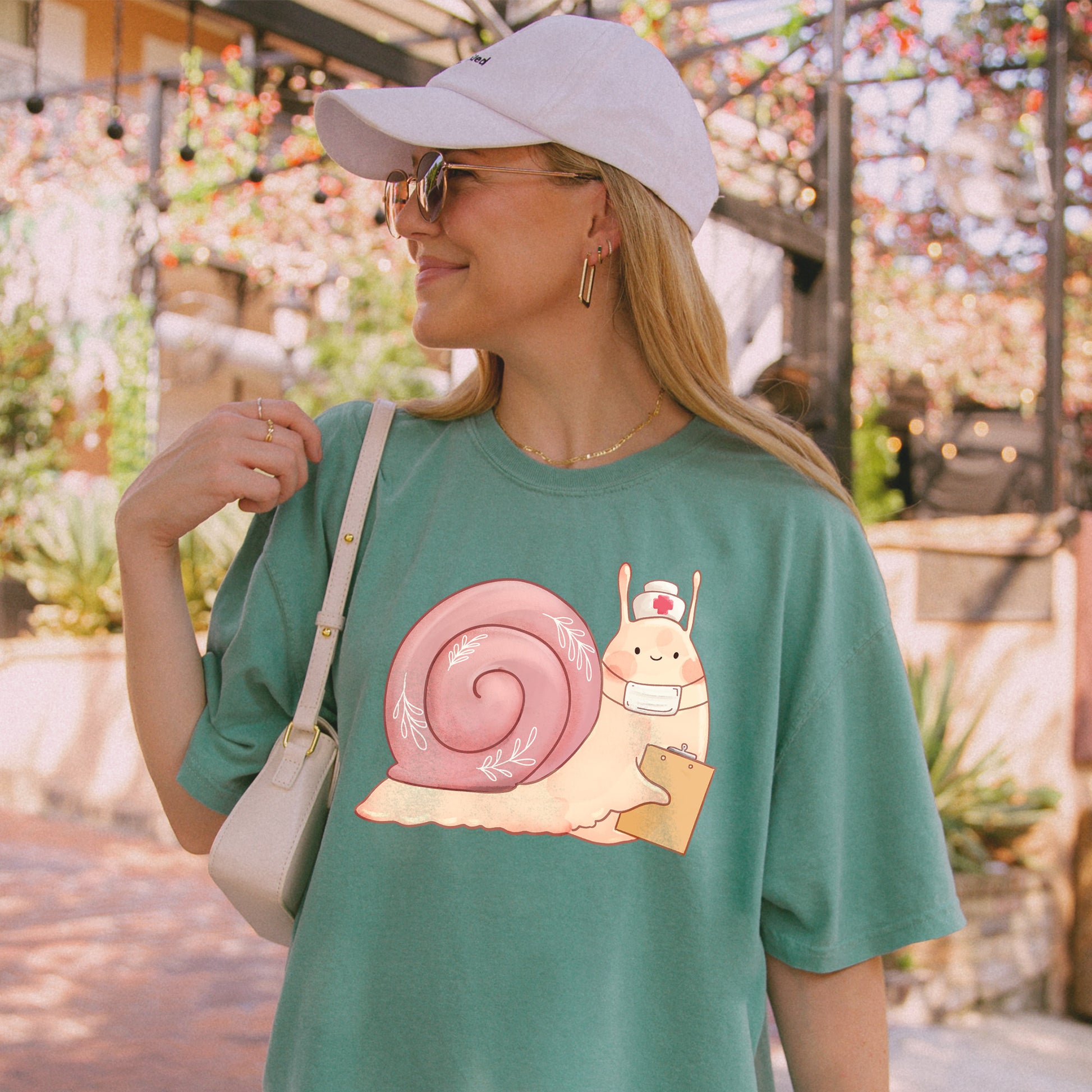 Woman wearing light green t-shirt with an illustration of snail holding a clipboard and wearing a nurse's hat and face mask.