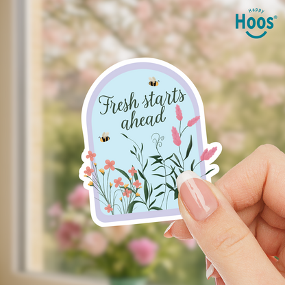 Hand holding a decorative sticker with floral design and 'Fresh starts ahead' text, with 'Happy Hoos' branding.