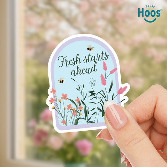 Hand holding a decorative sticker with floral design and 'Fresh starts ahead' text, with 'Happy Hoos' branding.
