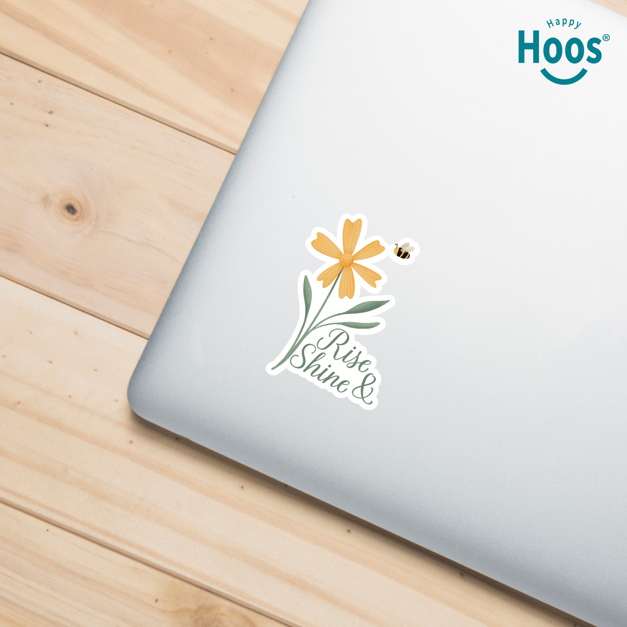 Laptop with a 'Rise & Shine' sticker on a wooden surface, featuring the 'Happy Hoos' brand.