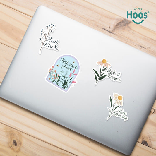 Laptop on a wooden surface with Motivation sticker pack with 4 floral design stickers  featuring the Hoos brand. The following text are presented in each sticker: Reset & Rise, Fresh Starts Ahead, make it Happen, Keep growing. 