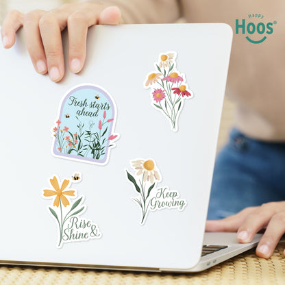 Laptop decorated with spring stickers: garden dome with "Fresh starts ahead", colorful wildflower bouquet, daisy with bee and "Rise & Shine", daisy with "Keep Growing"
