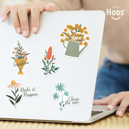 Summer stickers on laptop: flower bouquet with "Sunshine", coral botanical stem, yellow flowers in watering can, daisy with "Make it Happen", blue flowers with "Chase the sun"