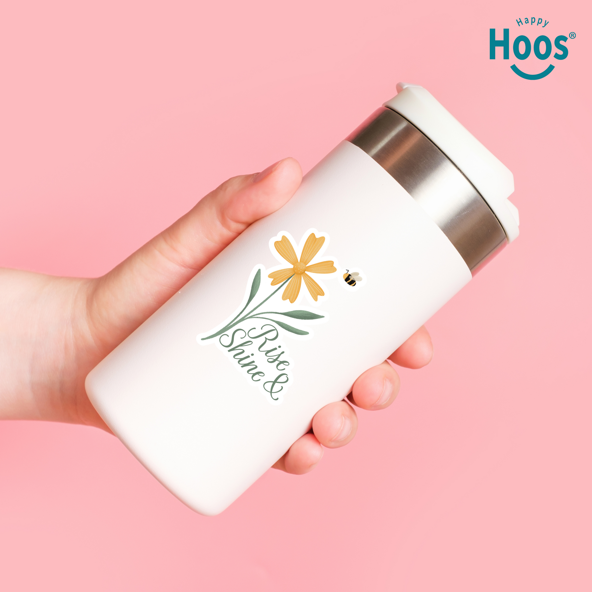 Hand holding a white tumbler with floral design and 'Happy Hoos' branding on a pink background