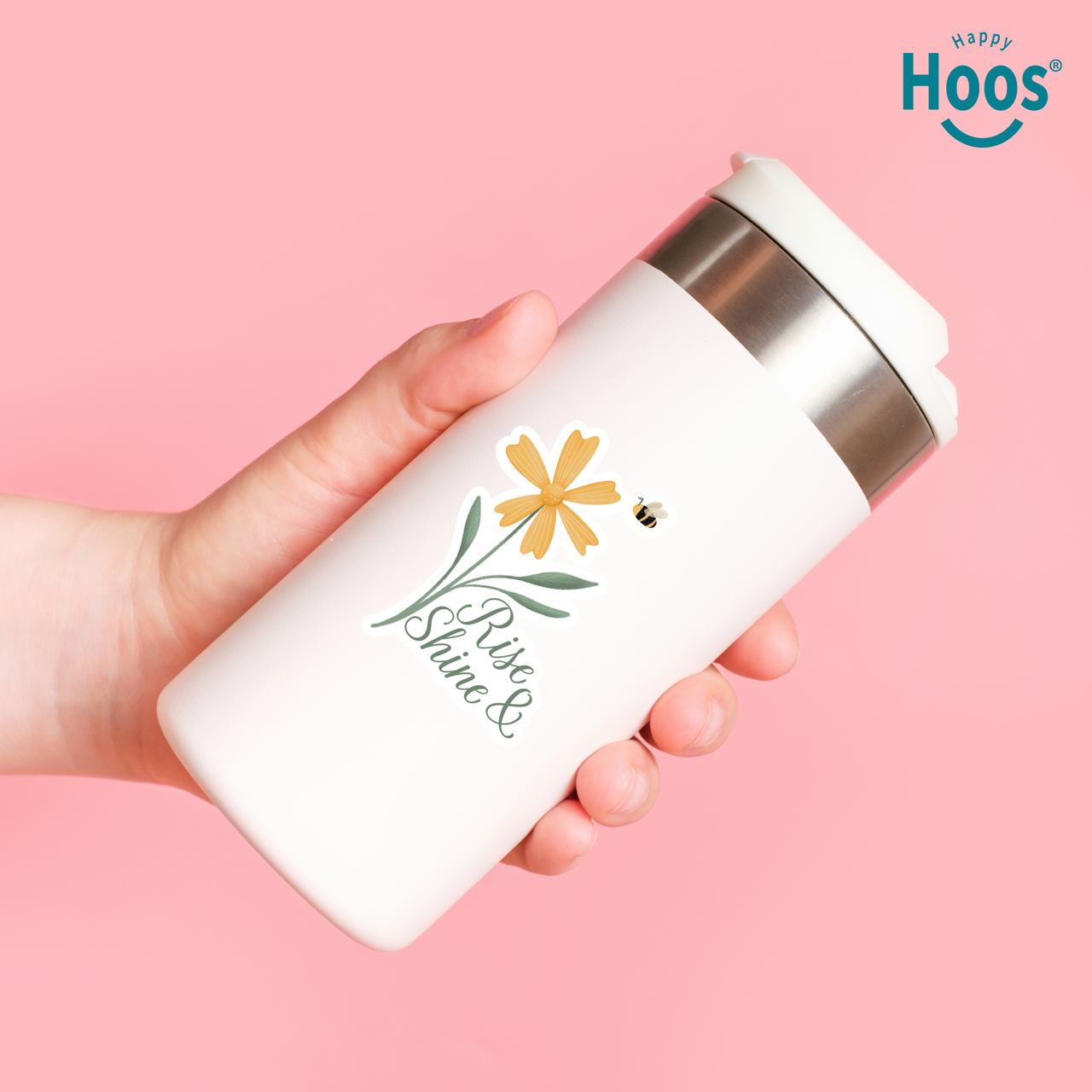 Hand holding a white tumbler with floral design and 'Happy Hoos' branding on a pink background