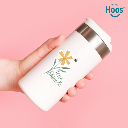 Hand holding a white tumbler with floral design and 'Happy Hoos' branding on a pink background