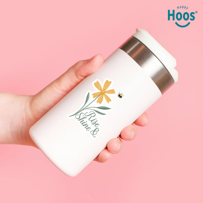 Hand holding a white tumbler with floral design and 'Happy Hoos' branding on a pink background