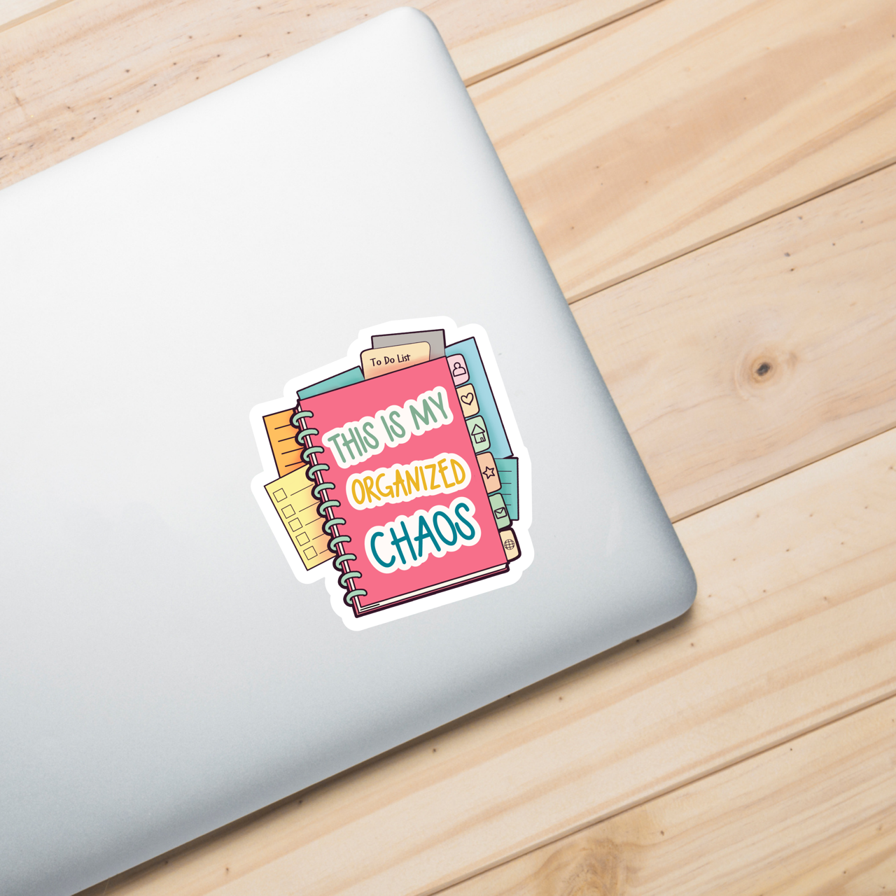 Laptop with a colorful sticker (This is my organized chaos) on a wooden surface