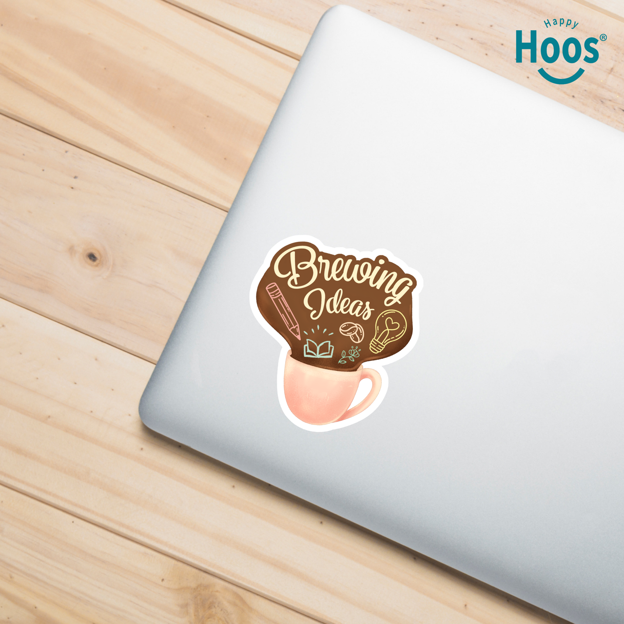 Laptop with a 'Brewing Ideas' sticker on a wooden surface, featuring the 'Happy Hoos' brand.