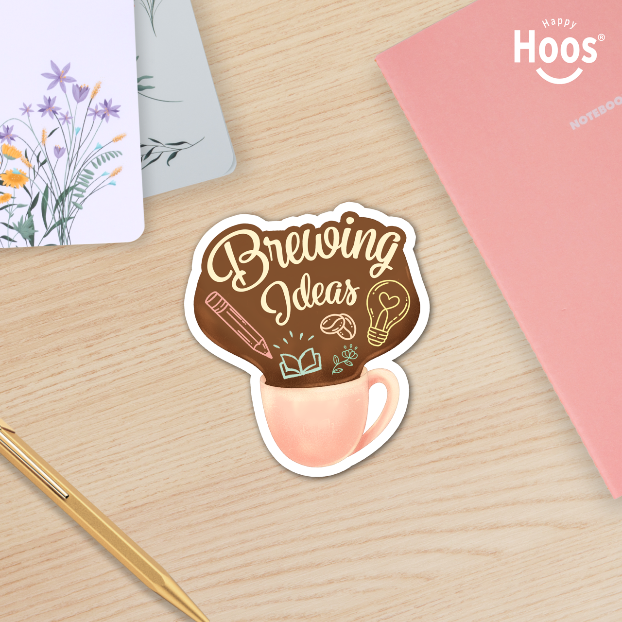 Sticker with 'Brewing Ideas' design on a wooden surface with Happy Hoos stationery items.
