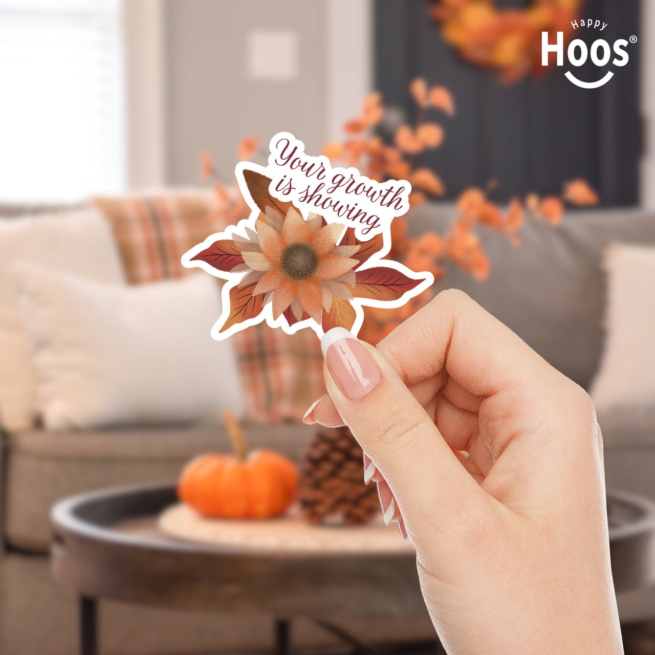 hand holding Autumn Growth sticker featuring a watercolor sunflower in autumn tones of orange, rust, and brown with fall leaves, and burgundy script lettering reading "Your growth is showing" at the top, measuring 3.3 by 2.9 inches
