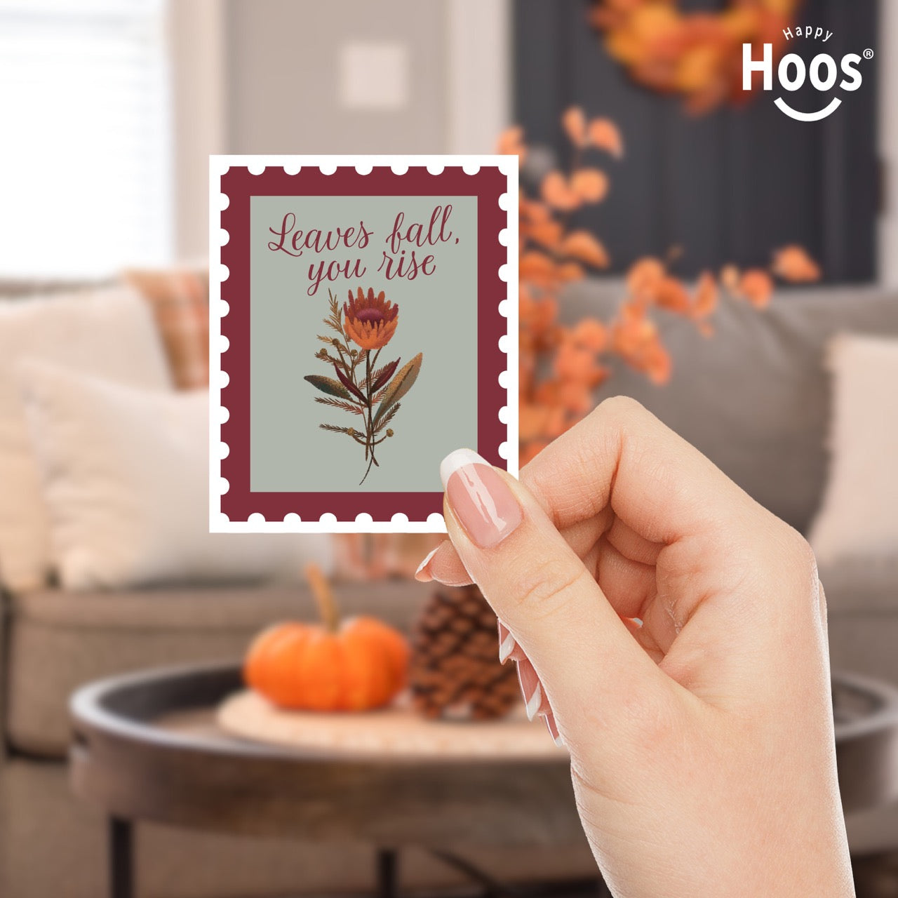 hand holding 
Fall & Rise sticker designed as a vintage postage stamp with burgundy perforated border, sage green background, featuring autumn botanicals with orange flowers and brown foliage, and burgundy script lettering reading "Leaves fall, you rise" at the top, measuring 2.5 by 3.3 inches

