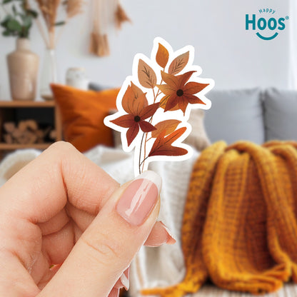 Woman holding Autumn Florals sticker featuring burnt orange and rust-colored flowers with star-shaped petals and matching autumn leaves arranged in a vertical floral spray, measuring 2.5 by 3.8 inches
