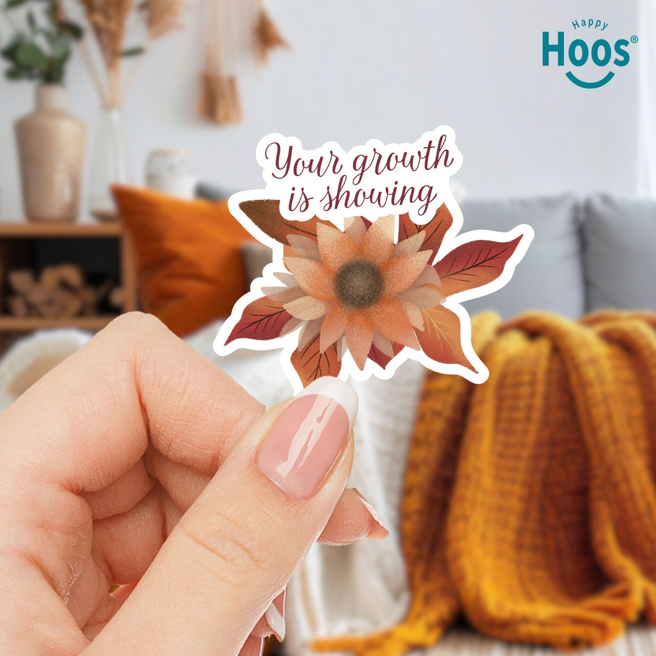 woman holding Autumn Growth sticker featuring a watercolor sunflower in autumn tones of orange, rust, and brown with fall leaves, and burgundy script lettering reading "Your growth is showing" at the top, measuring 3.3 by 2.9 inches