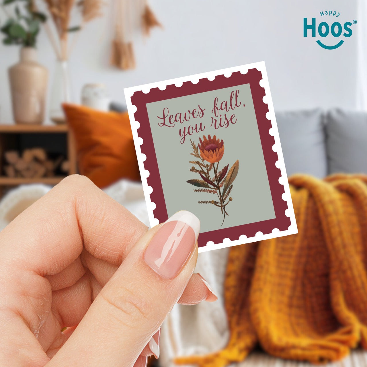 hand holding 
Fall & Rise sticker designed as a vintage postage stamp with burgundy perforated border, sage green background, featuring autumn botanicals with orange flowers and brown foliage, and burgundy script lettering reading "Leaves fall, you rise" at the top, measuring 2.5 by 3.3 inches