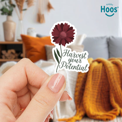 Hand holding Harvest Your Potential sticker featuring a deep burgundy gerbera daisy with detailed petals and green stem and leaves, with dark script lettering reading "Harvest your Potential" beside the flower, measuring 2.5 by 3.5 inches