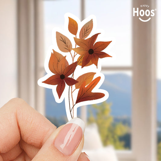 Hand holding a decorative sticker with autumn leaves and flowers, with 'Happy Hoos' logo in the corner.