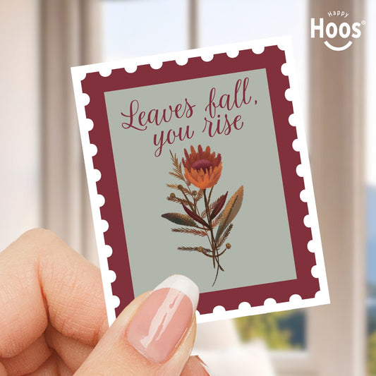 Sticker like a stamp with floral design and text 'Leaves fall, you rise' held by a hand, with 'Happy Hoos' branding.
