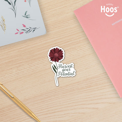 Harvest Your Potential sticker featuring a deep burgundy gerbera daisy with detailed petals and green stem and leaves, with dark script lettering reading "Harvest your Potential" beside the flower, measuring 2.5 by 3.5 inches surrounded by Happy Hoos Notebooks