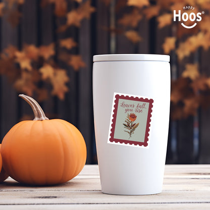 White tumbler with a fall-themed label next to a pumpkin on a wooden surface.