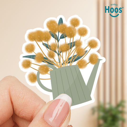 Sticker of a green watering can with yellow flowers held by a hand against a beige background.