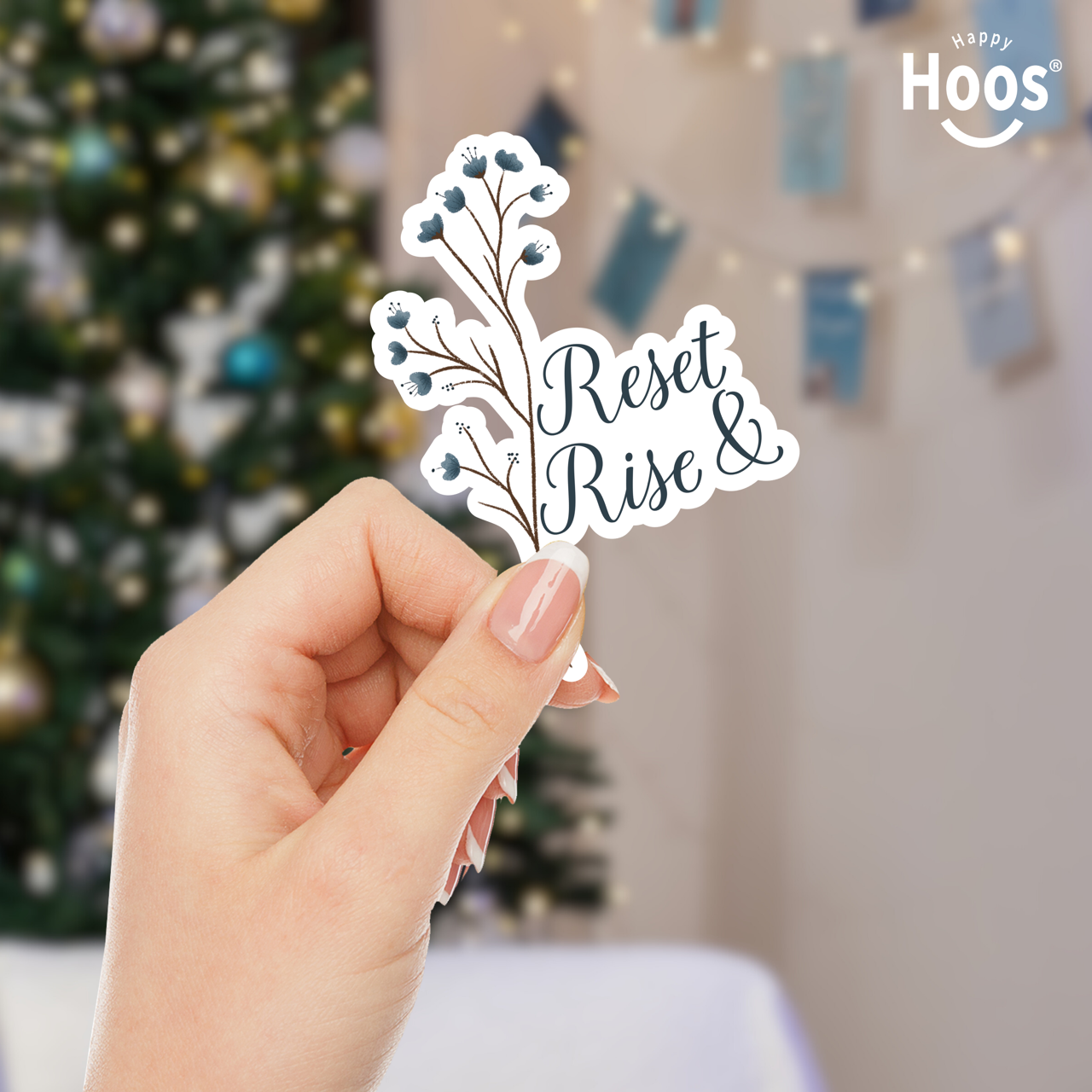 Hand holding a decorative cutout with 'Reset & Rise' text in front of a Christmas tree.