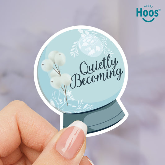 Round sticker with 'Quietly Becoming' text and floral design held by a hand, with 'Happy Hoos' logo in the corner.