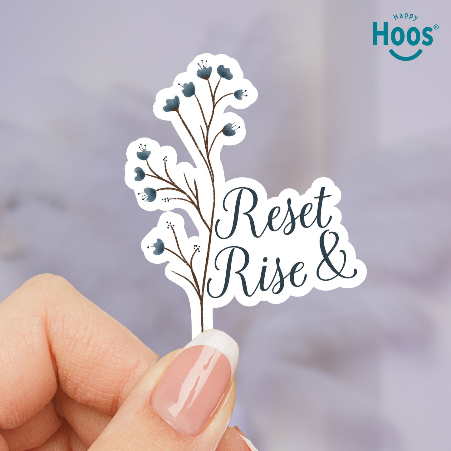 Hand holding a sticker with 'Reset & Rise' text and floral design, blurred indoor background