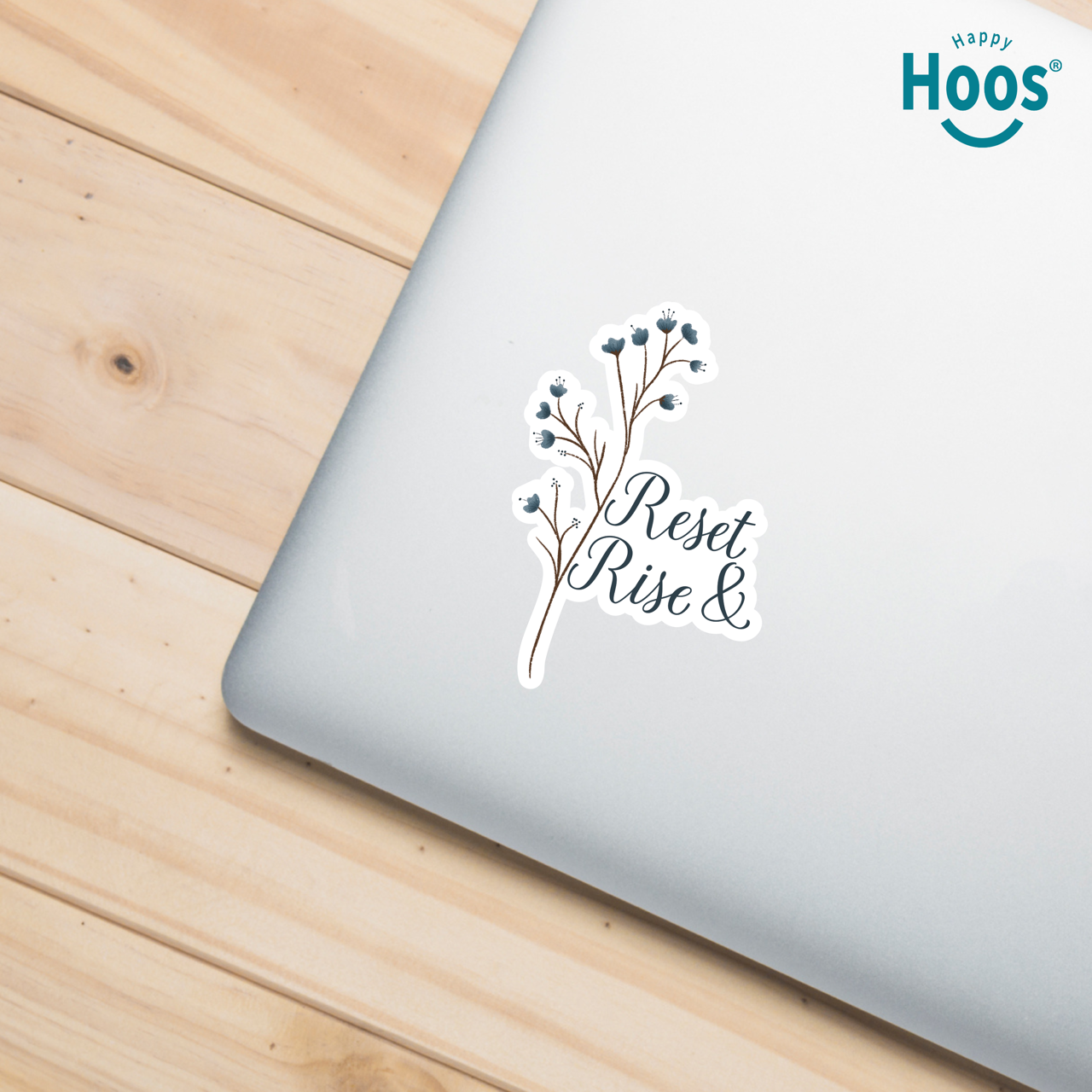 Laptop with a motivational sticker on a wooden surface, featuring the brand 'Happy Hoos'.