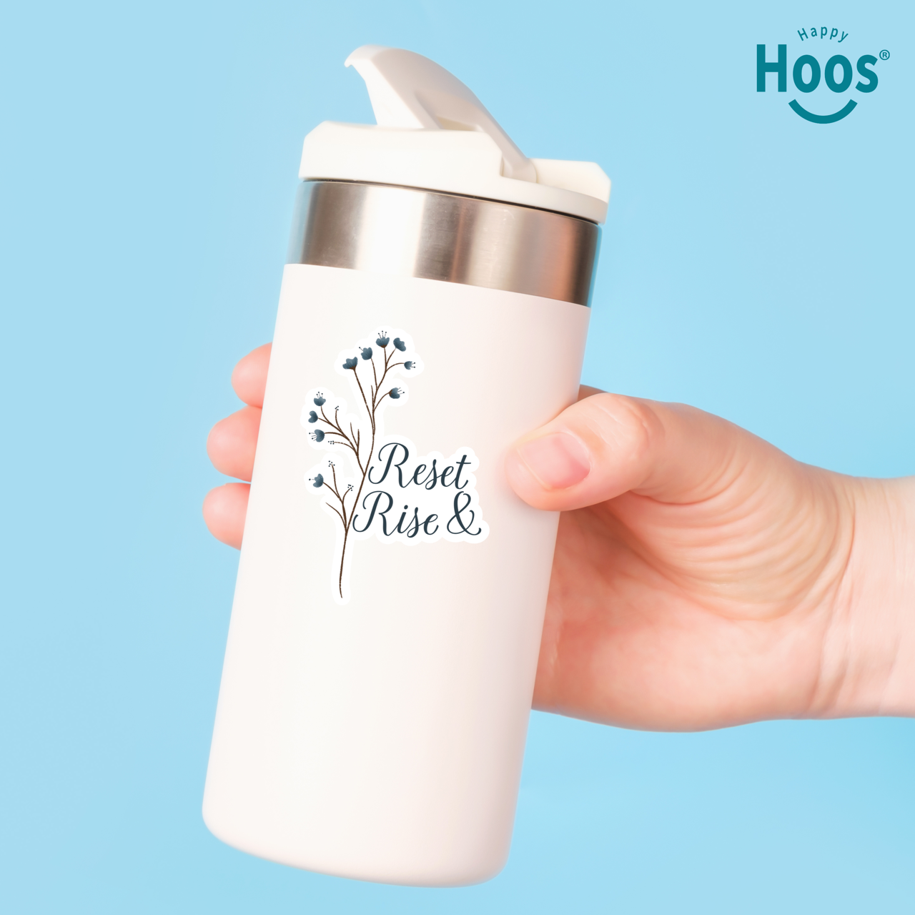 White travel mug with 'Reset & Rise' text and floral design, held against a blue background with 'Happy Hoos' branding.