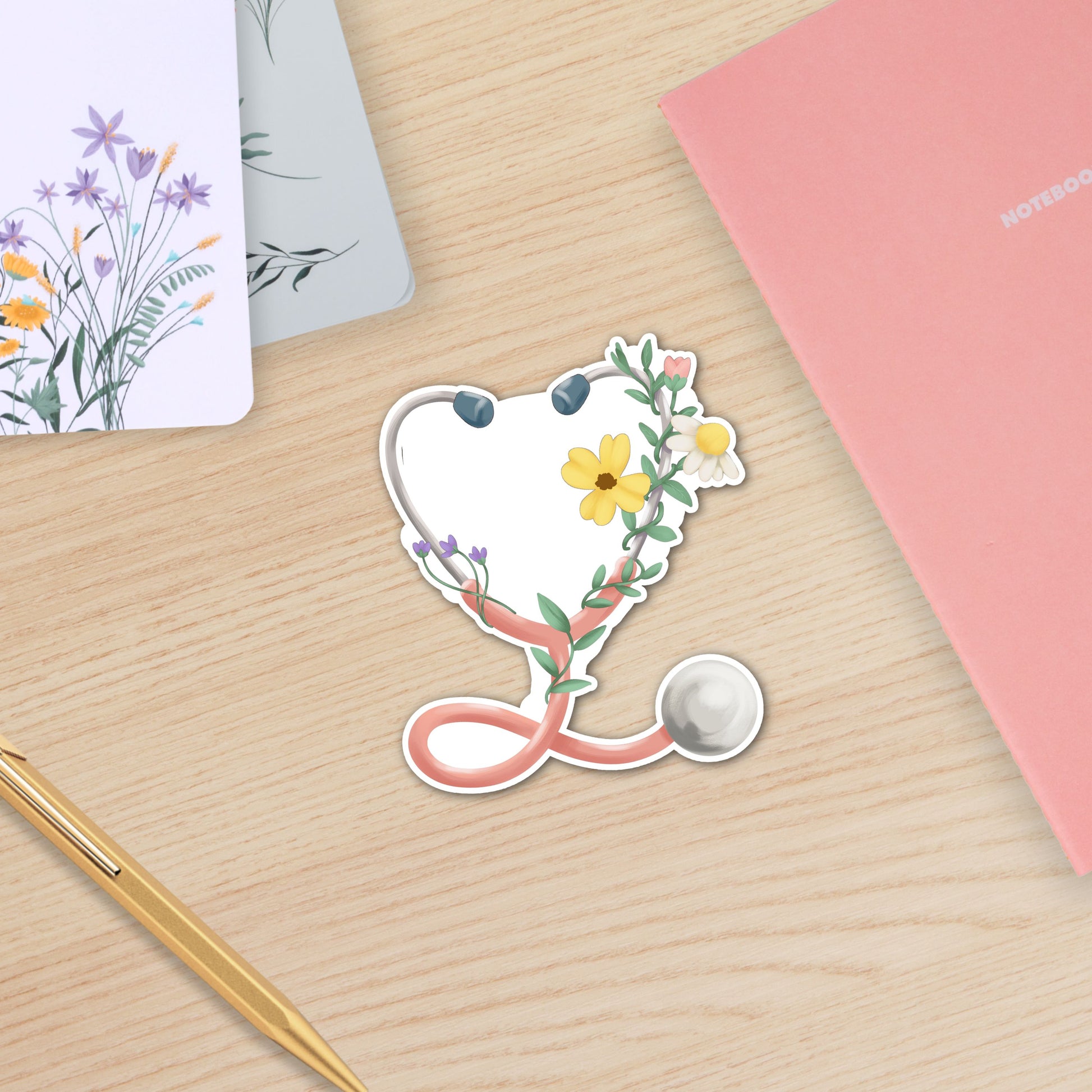 Floral Stethoscope waterproof sticker featuring a pink stethoscope wrapped with flowers and greenery for nurses and healthcare workers on wooden table