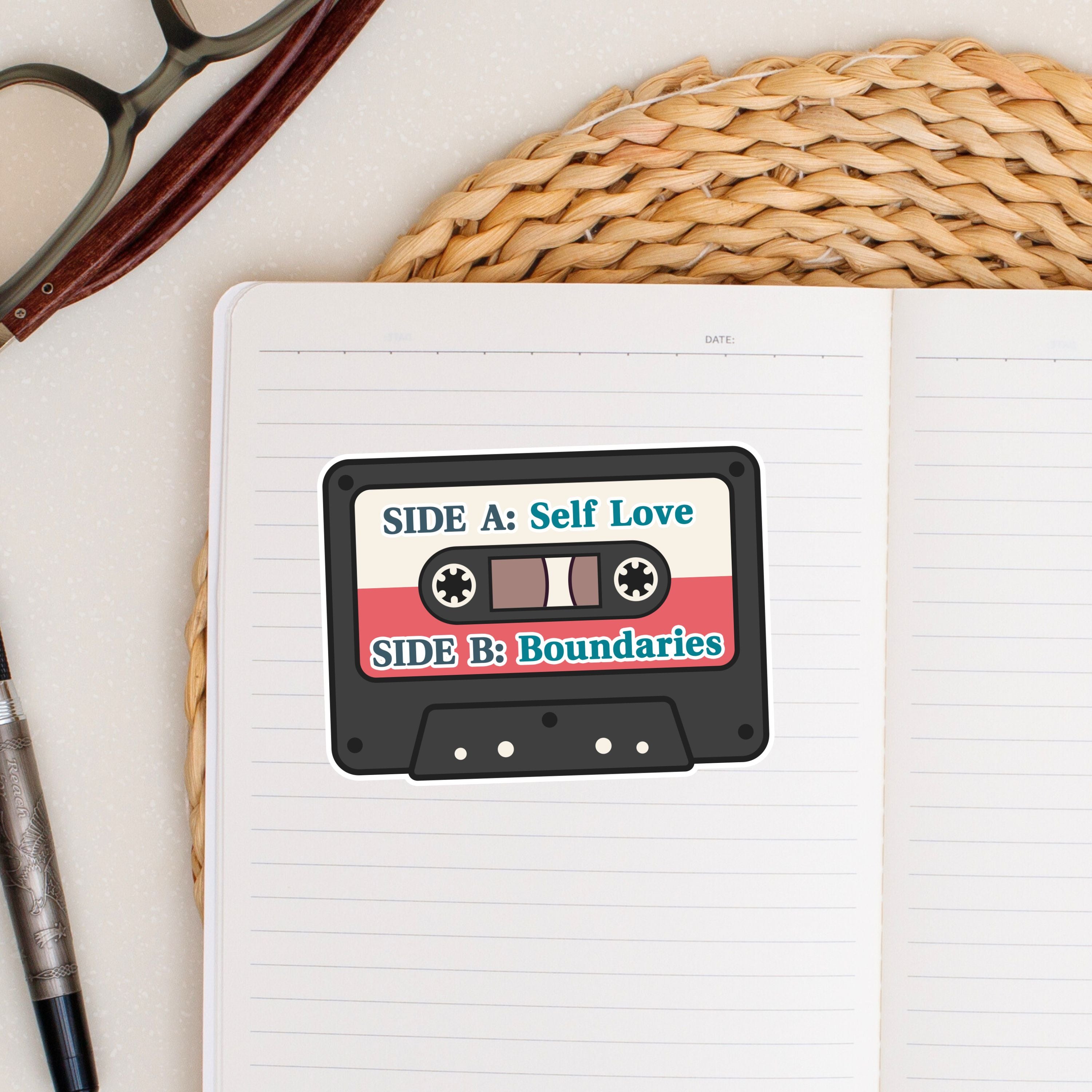 Cassette tape design on a notebook with 'Self Love' and 'Boundaries' text, placed on a textured surface with glasses and pen.