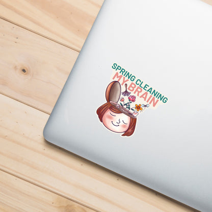 Spring Cleaning My Brain waterproof sticker on a laptop featuring a smiling face with flowers growing from an open head, made for self care, overthinkers, mental reset, planners, laptops, and water bottles.